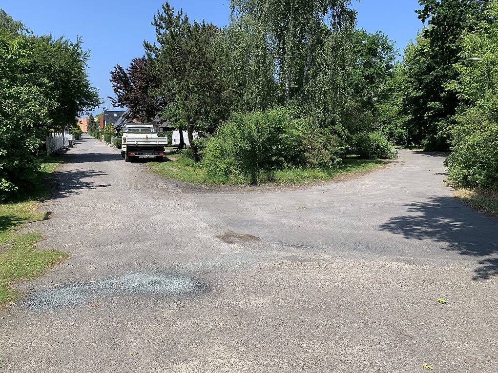 Gabelung einer kaputten Straße zwischen grünen Büschen und Bäumen unter blauem Himmel
