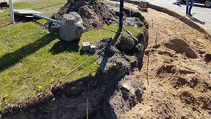 Baustelle mit aufgerissenem Erdreich neben einer Straße, auf der ein Bauarbeiter in Warnweste steht