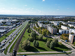 Luftaufnahme einer Stadt mit Autobahn, Bahngleisen, Grünflächen und Wohngebäuden unter blauem Himmel