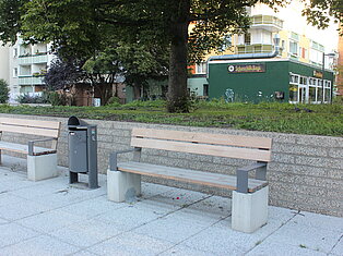 Zwei leere Sitzbänke auf gepflasterten Untergund.