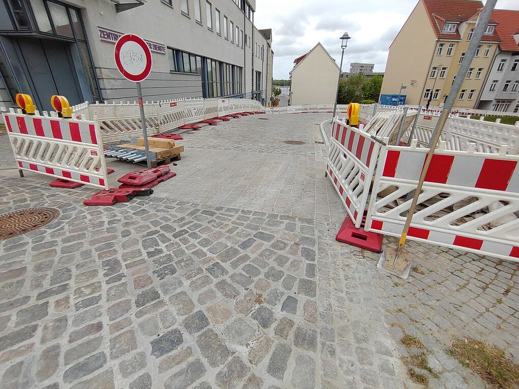 Sanierte gepflasterte Straße mit Absperrung.