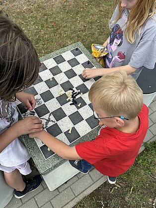 Drei Kinder spielen Schach an einem Marmor-Schachtisch im Freien