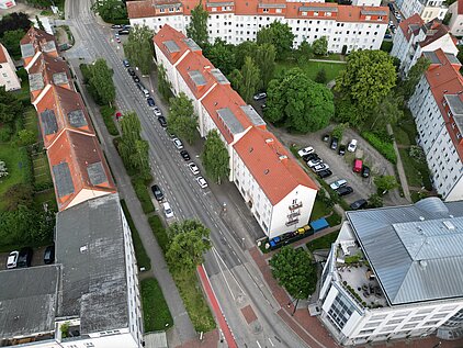 Luftaufnahme einer Straße mit Straßenbahn, umgeben von mehrstöckigen Wohngebäuden und Bäumen.