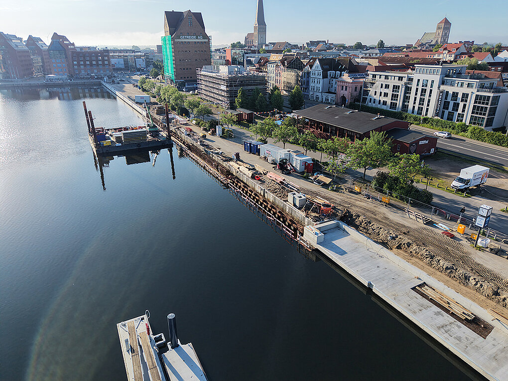 Luftaufnahme eines Stadthafens mit Bauarbeiten an der Uferpromenade und Gebäuden im Hintergrund