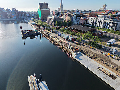 Luftaufnahme eines Stadthafens mit Bauarbeiten an der Uferpromenade und Gebäuden im Hintergrund