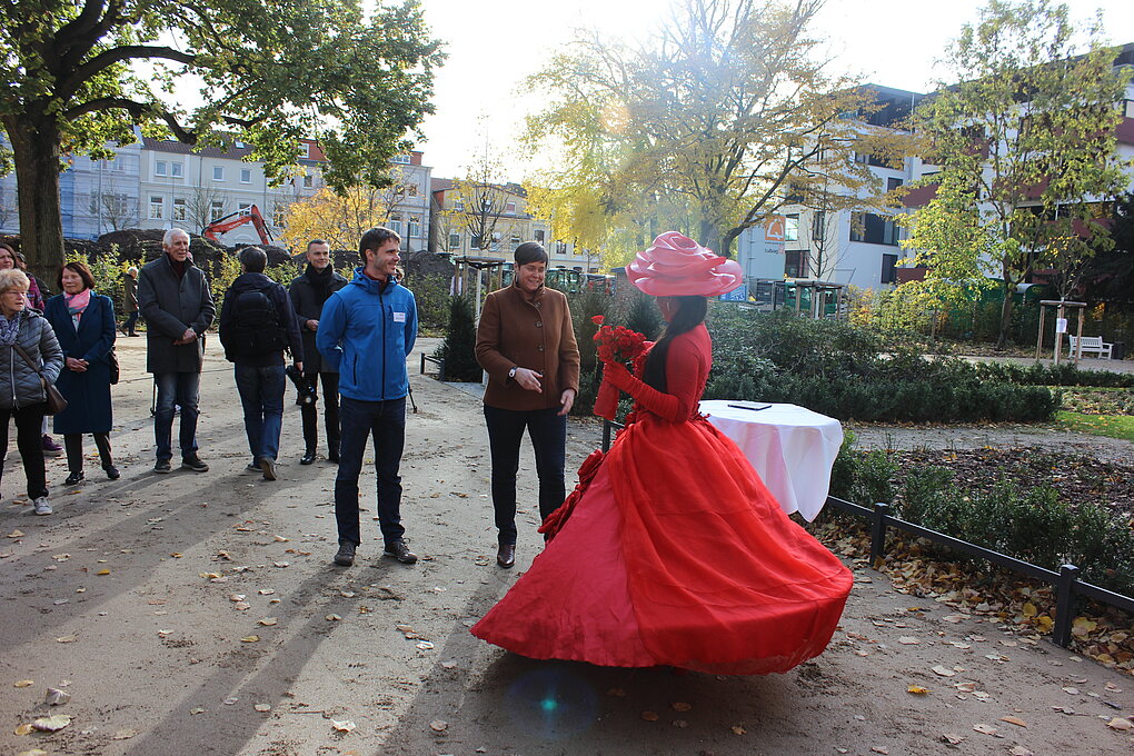 Menschen beobachten eine Frau in einem roten Kleid, die auf einer Straße tanzt