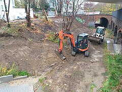 Fläche mit Bäumen und Sträuchern und zwei Baufahrzeugen.