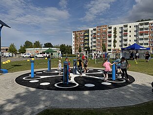 Kinder spielen auf einem Spielplatz vor einem Wohngebäude bei bewölktem Himmel