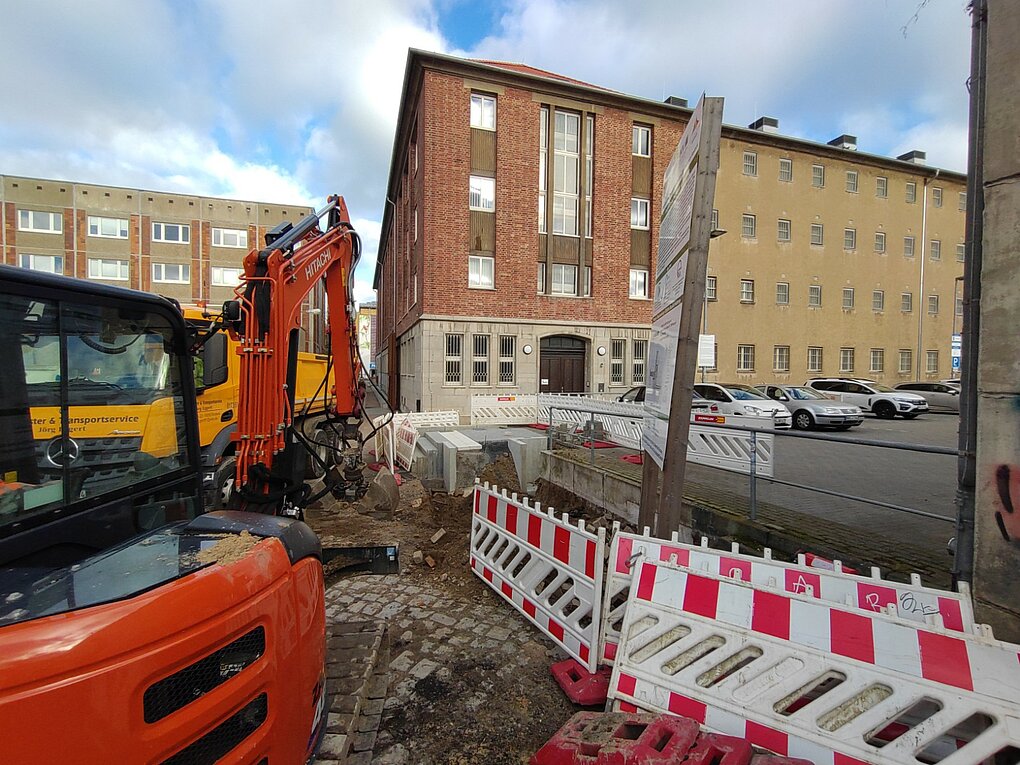 Baustelle mit Absperrungen und einem orangefarbenen Fahrzeug vor einem Backsteingebäude
