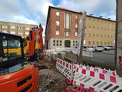 Baustelle mit Absperrungen und einem orangefarbenen Fahrzeug vor einem Backsteingebäude