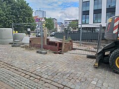 Blick auf eine eingezäunte kleine Baustelle mit Baugeräten im Boden..