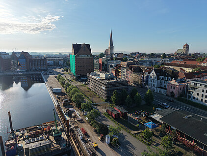 Stadthafen mit Wasserbecken links, Baustelle und Gebäuden in der Stadt mit Kirchturm im Hintergrund bei klarem Himmel