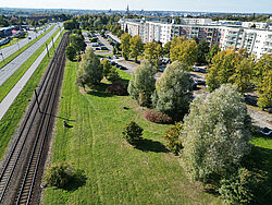 Luftaufnahme eines Wohngebiets mit mehrstöckigen Häusern, Parkplätzen, Bäumen und einem parallel verlaufenden Bahngleis