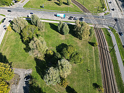 Luftaufnahme eines Bahngleises neben einem Parkplatz mit mehreren Autos und einem Wohngebäude