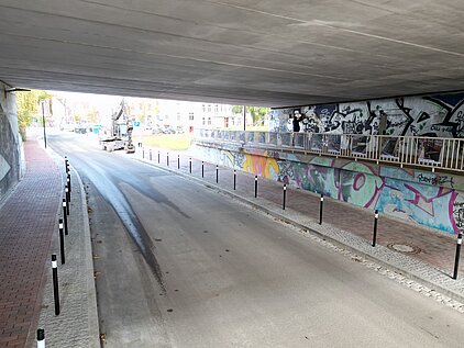 Straße unter einer Brücke mit mehreren Pfosten entlang des Gehwegs