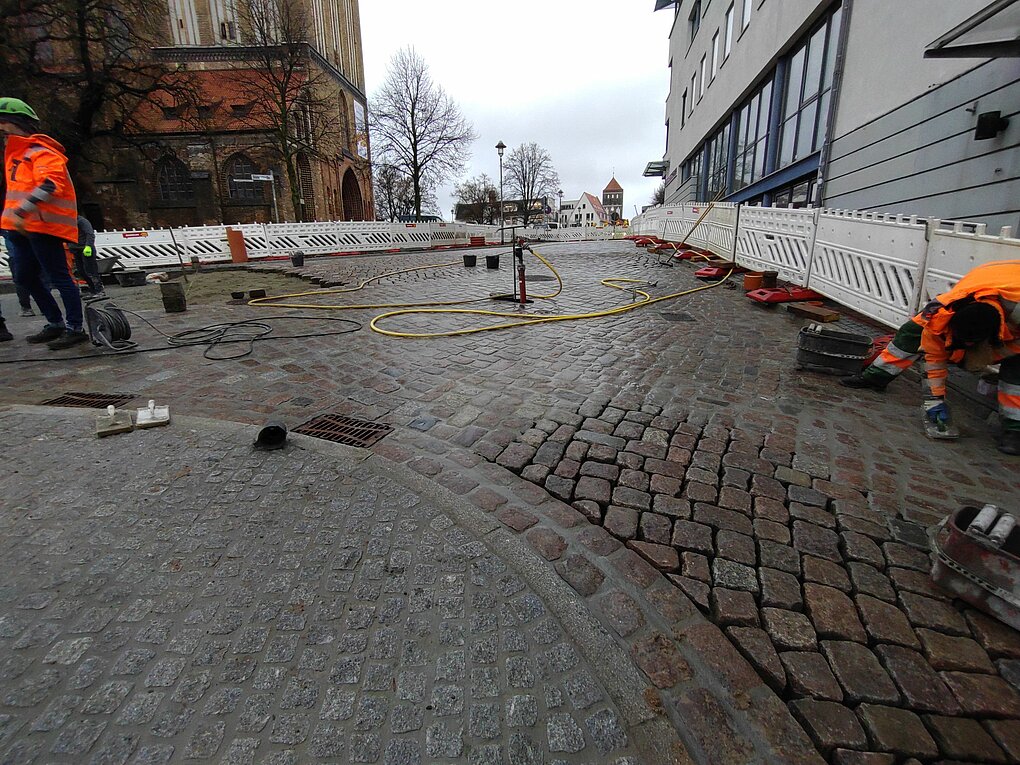 Bauarbeiter auf einem gepflasterten Platz an einem bewölktem Tag.