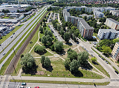 Luftaufnahme eines dreieckigen Parks mit Wegen und Bäumen neben Wohngebäuden und einer Straße mit Bahngleisen