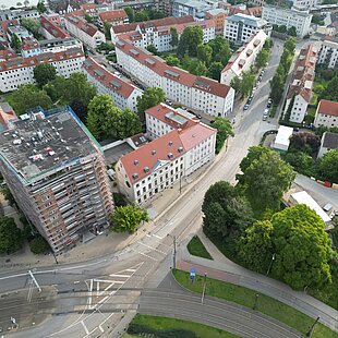Luftaufnahme einer Kreuzung mit mehreren Straßen, umgeben von Gebäuden und Bäumen.