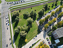 Luftaufnahme eines dreieckigen Grünstreifens mit Bäumen zwischen Straßen und einem Parkplatz neben einem mehrstöckigen Gebäude