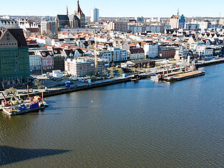 Stadthafen mit Wasserfront, Bauarbeiten an Pontons, dahinter historische und moderne Gebäude der Innenstadt bei klarem Himmel