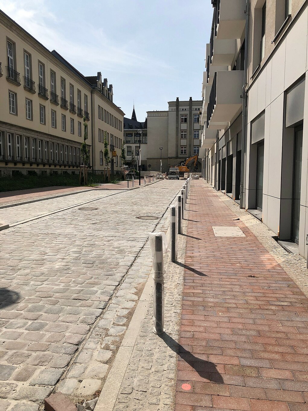 Sanierte Straße und Gehwege mit Baufahrzeugen im Hintergrund.
