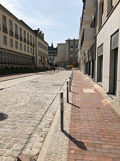 Sanierte Straße und Gehwege mit Baufahrzeugen im Hintergrund.