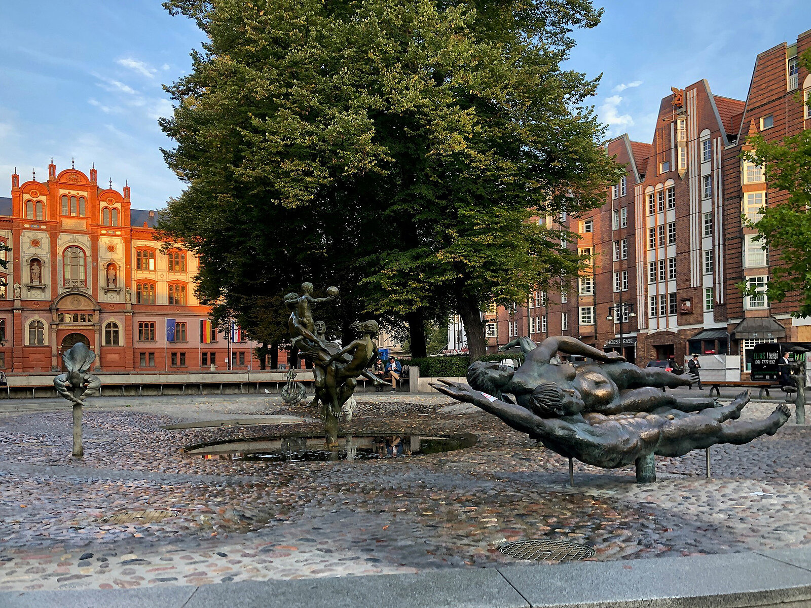 Städtischer Platz mit Bänken, Bäumen und Gebäuden im Hintergrund bei klarem Himmel