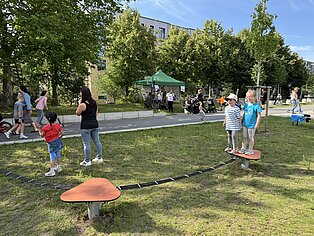 Kinder spielen auf einer Wippe in einem Park mit Bäumen und einem Pavillon im Hintergrund