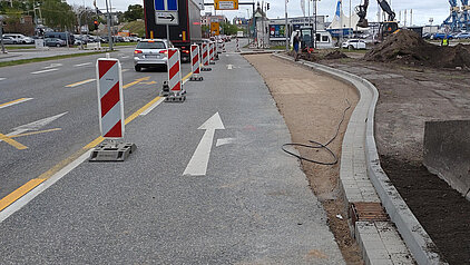 Straße mit Baustellenabsperrungen und einem weißen Pfeil auf dem Asphalt, der geradeaus weist