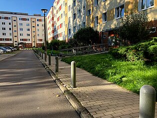 Straße mit Gehwegen und zahlreichen Wohnblöcken.