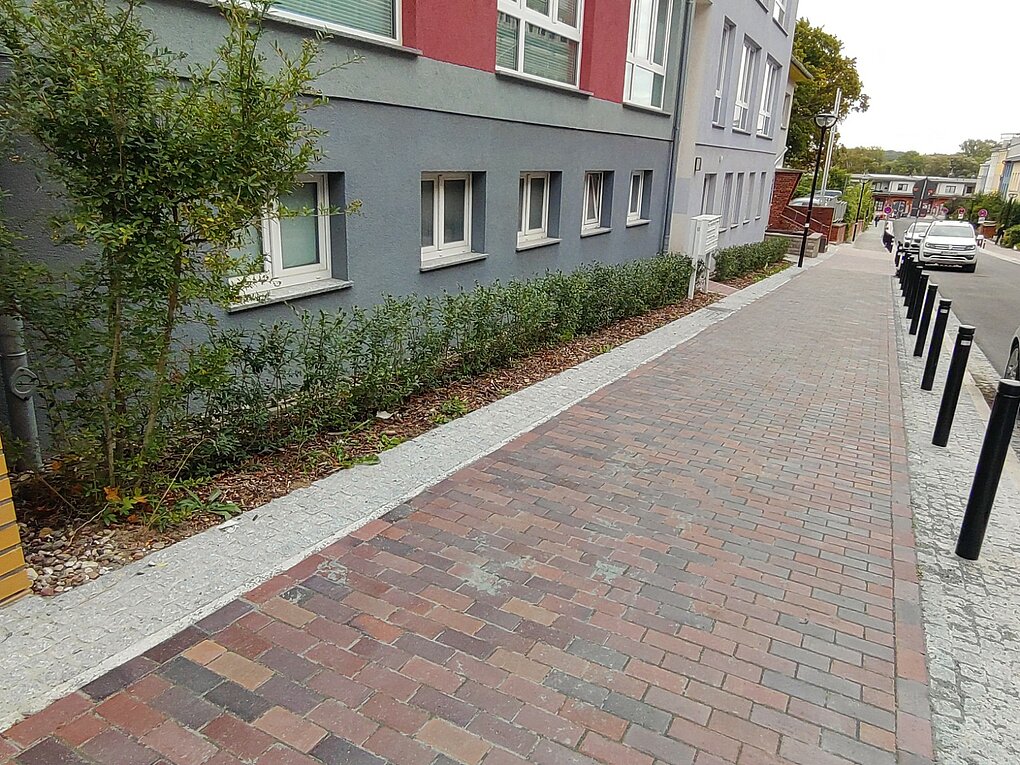Blick eine Straße hinuter mit Gehweh und parkenden Autos.