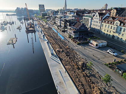 Luftaufnahme eines Stadthafens mit Bauarbeiten an der Uferpromenade und angrenzenden Gebäuden