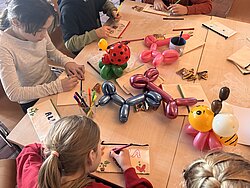 Mehrere Personen sitzen an einem Tisch und arbeiten mit buntem Bastelmaterial