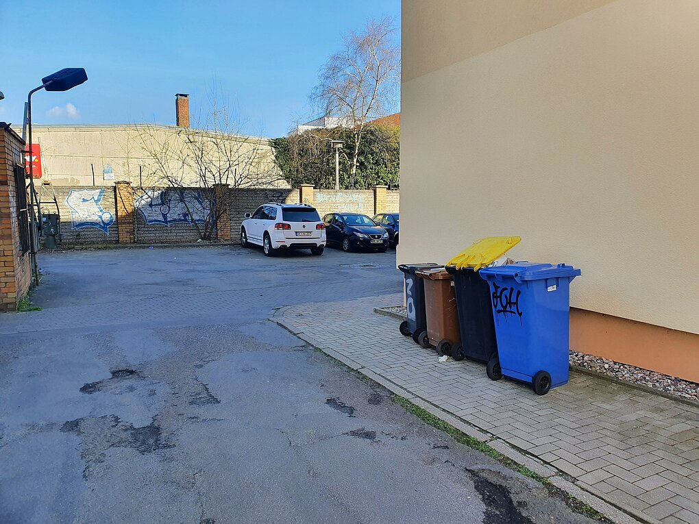 Blick auf eine kaputte Straße mit parkenden Autos im Hintergrund.