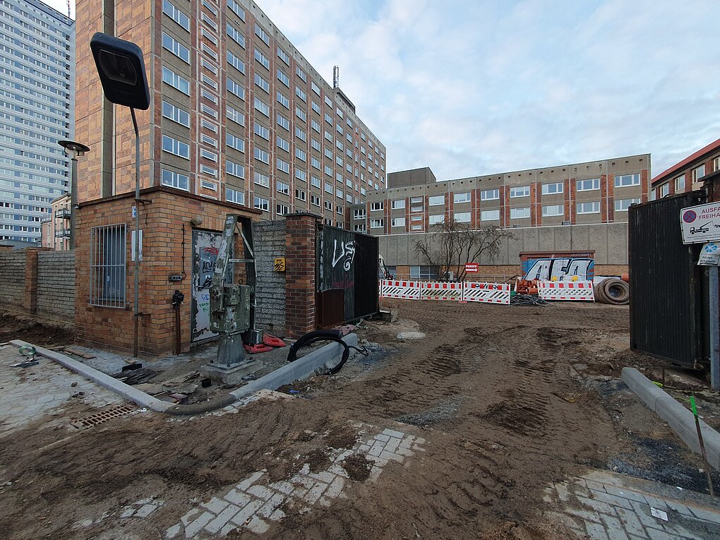 Baustelle mit Gebäuden im Hintergrund unter bewölktem Himmel