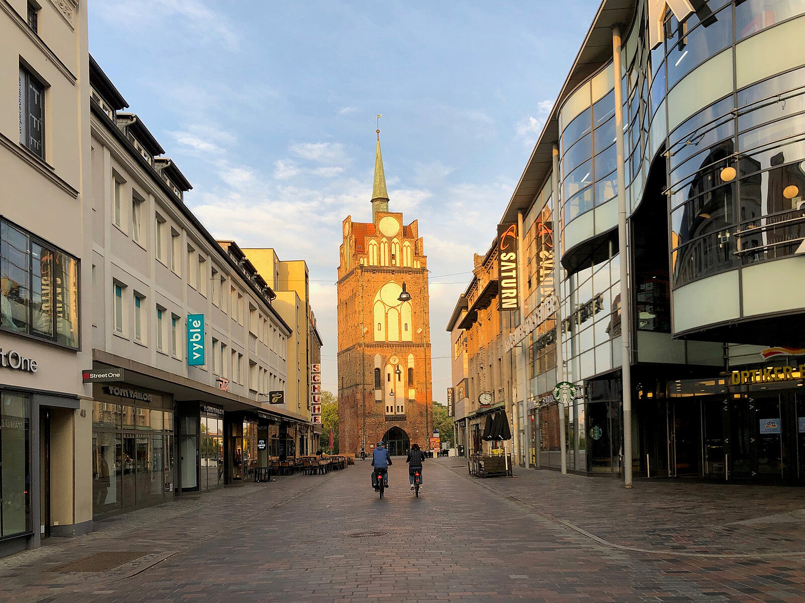 Straße mit historischen Gebäuden mit dem Kröpeliner Tor im Hintergrund bei klarem Himmel