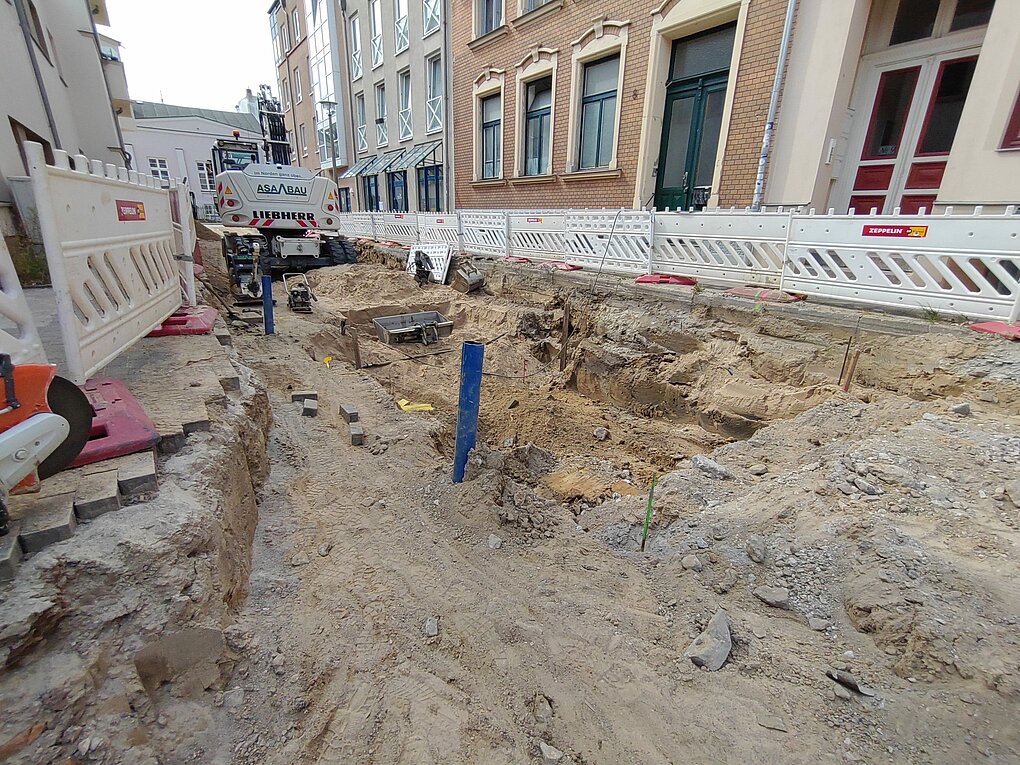 Baustelle mit aufgerissenem Boden und Baumaterialien vor einem Gebäude